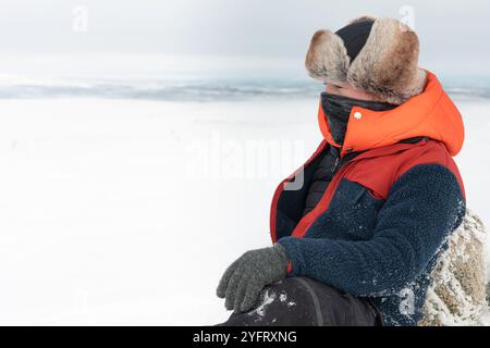 Musher maschile caucasico adulto vestito con attrezzatura artica su un paesaggio innevato di tundra, di fronte a freddo estremo, in una natura selvaggia ghiacciata, slitte trainate da cani in bac Foto Stock