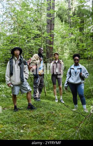 Gruppo multietnico di turisti che si trovano all'aperto sul sentiero della foresta e guardano la macchina fotografica mentre camminano insieme Foto Stock