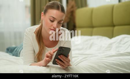 Donna caucasica donna signora a casa camera da letto rilassarsi utilizzando il telefono cellulare navigare sui social media coreano asiatico amico ragazza saltare sul letto menzogna amici parlare Foto Stock