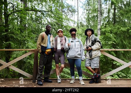 Ritratto a figura intera di un gruppo multietnico di giovani come turisti in natura che guardano la macchina fotografica in piedi sul ponte con uno splendido paesaggio sullo sfondo Foto Stock