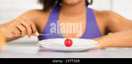 Afro donna che guarda il pomodoro piccolo su un piatto Foto Stock