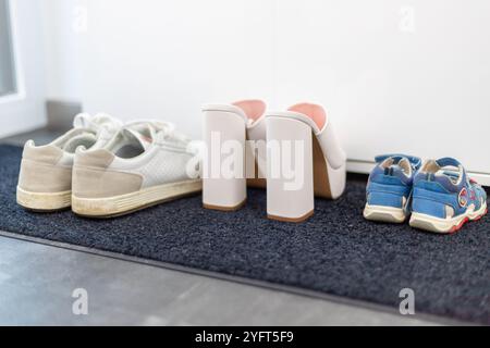 Scarpe da famiglia davanti a un armadio, sneakers da uomo, scarpe da bambino e tacchi alti bianchi. Foto di alta qualità Foto Stock