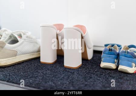 Scarpe da famiglia davanti a un armadio, sneakers da uomo, scarpe da bambino e tacchi alti bianchi. Foto di alta qualità Foto Stock