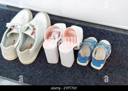 Scarpe da famiglia davanti a un armadio, sneakers da uomo, scarpe da bambino e tacchi alti bianchi. Foto di alta qualità Foto Stock