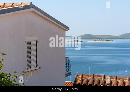 Vista sul mare dalla casa mediterranea con persiane chiuse e isole oceaniche sullo sfondo nelle giornate di sole. Concetto di vita costiera, pacifico Foto Stock