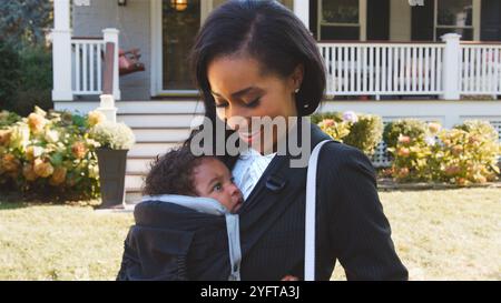 Donna d'affari che porta il bambino a Papoose Sling che lascia la casa per lavoro Foto Stock