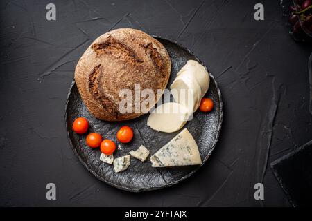 Formaggi assortiti. Mozzarella e garganzola blu con pane di segale scuro e pomodori ciliegini con basilico verde su un piatto di mica nera su sfondo scuro. Foto di alta qualità Foto Stock