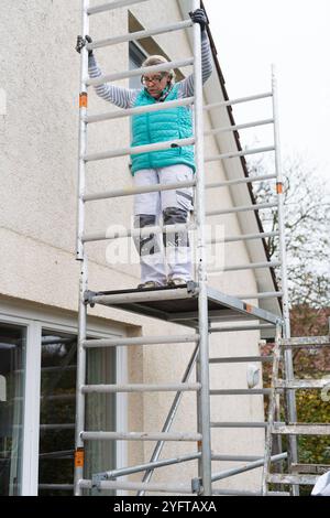 Gerüstbauerin, Malerin baut ein mobiles Gerüst am Einfamilienhaus auf, modello rilasciato für redaktionelle Nutzung, Gerüstbauer *** Scaffolder, pittore erige ponteggi mobili su una casa indipendente, modello rilasciato per uso editoriale, ponteggio 20241105-DSC 8691 Foto Stock