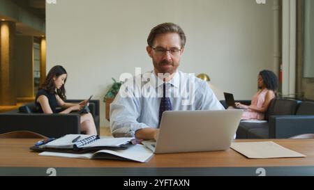 Uomo d'affari maturo in un'area salotto informale dell'ufficio moderno che lavora su un notebook Foto Stock