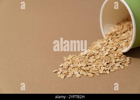 Farina d'avena versata dal contenitore di carta su sfondo marrone, primo piano con spazio di copia Foto Stock