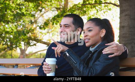 Coppia giovane amorevole all'aperto sul Park Bench con caffè da asporto Foto Stock