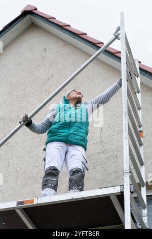 Gerüstbauerin, Malerin baut ein mobiles Gerüst am Einfamilienhaus auf, modello rilasciato für redaktionelle Nutzung, Gerüstbauer *** Scaffolder, pittore erige ponteggi mobili su una casa indipendente, modello rilasciato per uso editoriale, ponteggio 20241105-DSC 8723 Foto Stock