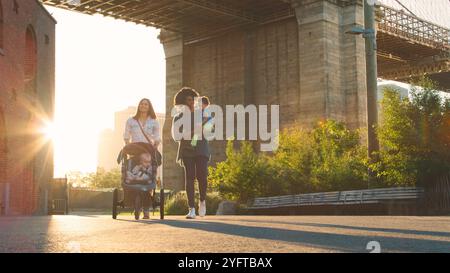 Giornata in famiglia a New York con due mamme a piedi sul ponte di Brooklyn con bambini Foto Stock