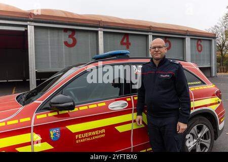 Stadtallendorf, Germania. 5 novembre 2024. L'ispettore dei vigili del fuoco della città Patrick Schulz si trova di fronte alla sala leggera in parte del parcheggio dell'Herrenwaldstadion, che funge da parcheggio temporaneo per i vigili del fuoco di Stadtallendorf. Il 16 ottobre, la nuova sala veicoli presso la sede dei vigili del fuoco, in cui si erano trasferiti solo lo scorso dicembre, è bruciata insieme ai veicoli. Crediti: Christian Lademann/dpa/Alamy Live News Foto Stock
