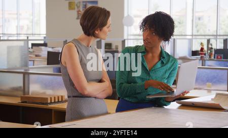 Due architetti femminili che si incontrano in un moderno ufficio open plan studiando progetti o disegni di edifici Foto Stock