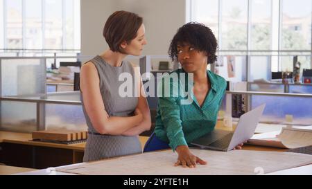 Due architetti femminili che si incontrano in un moderno ufficio open plan studiando progetti o disegni di edifici Foto Stock