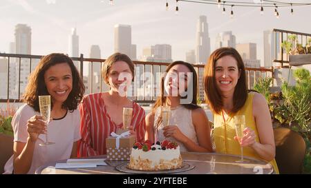 Ritratto di amiche che celebrano il compleanno sulla terrazza sul tetto con skyline della città sullo sfondo Foto Stock