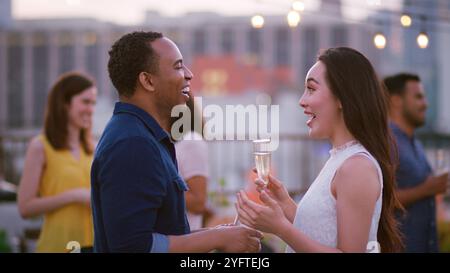 Gli amici si sono riuniti sulla terrazza sul tetto per una festa serale con lo skyline della città sullo sfondo Foto Stock