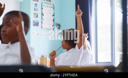 Gruppo di alunni elementari in uniforme in classe scolastica alzando la mano per rispondere alla domanda Foto Stock