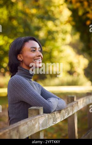 Vista profilo di una giovane donna a piedi nella campagna autunnale appoggiata sul recinto Foto Stock