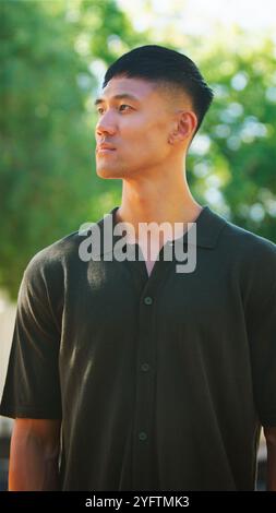 Un giovane uomo è in piedi all'aperto, guardando da un lato con un'espressione premurosa. La luce del sole illumina dolcemente il suo volto, evidenziando le sue caratteristiche Foto Stock