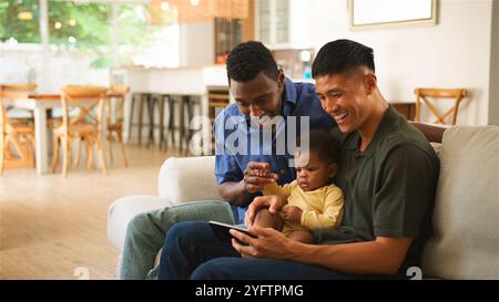 Due adulti e un bambino si divertono con un tablet, condividendo i sorrisi in uno spazio accogliente. Foto Stock