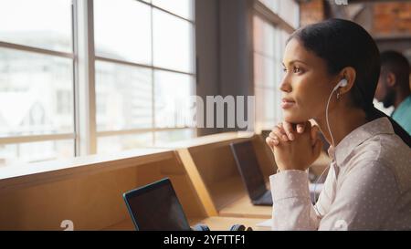 Donna d'affari che lavora in un moderno ufficio multiculturale ascoltando musica con auricolari o auricolari Foto Stock