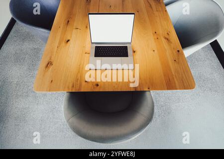 computer portatile con mockup a schermo bianco vuoto, sala meeting interna con comode poltrone e tavolo in legno Foto Stock