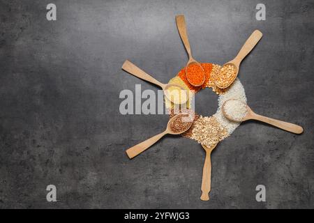 Diversi tipi di cereali e legumi in cucchiai di legno su tavola grigia, piatti. Spazio per il testo Foto Stock