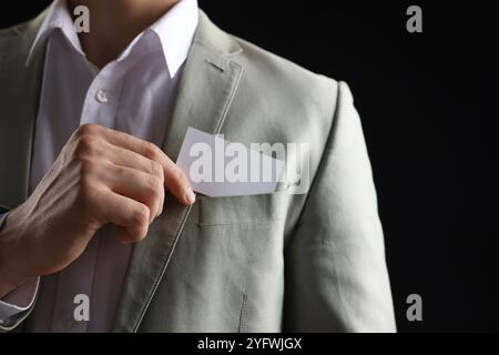 Uomo che prende un biglietto da visita vuoto dalla tasca della giacca su sfondo nero, primo piano. Mockup per il design Foto Stock