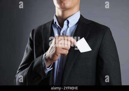 Uomo che prende un biglietto da visita vuoto dalla tasca della giacca su sfondo grigio, primo piano. Mockup per il design Foto Stock