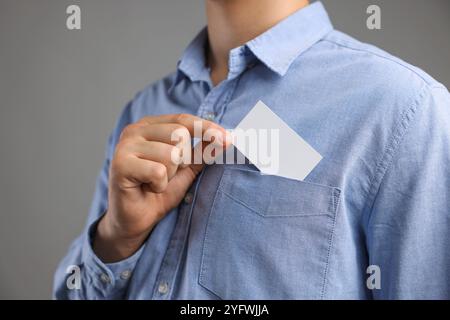 Uomo che prende un biglietto da visita vuoto dalla tasca della giacca su sfondo grigio, primo piano. Mockup per il design Foto Stock