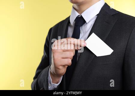 Uomo che prende un biglietto da visita vuoto dalla tasca della giacca su sfondo giallo, primo piano. Mockup per il design Foto Stock