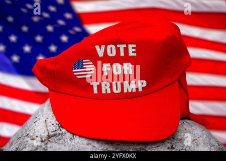 5 novembre 2024: Immagine simbolica per il sostegno di Donald Trump alle elezioni americane - un cappello rosso con l'iscrizione: VOTA PER TRUMP, davanti a una bandiera americana. FOTOMONTAGGIO *** Symbolbild für Unterstützung von Donald Trump bei den US-Wahlen - eine rote Kappe mit der Aufschrift: VOTA PER TRUMP, vor einer amerikanischen Flagge. FOTOMONTAGE Foto Stock