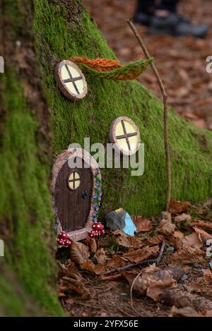 Una foto ravvicinata di un'affascinante porta delle fate in miniatura annidata contro un tronco di albero coperto di muschio, nel profondo di una foresta autunnale. Circondato da caduti Foto Stock