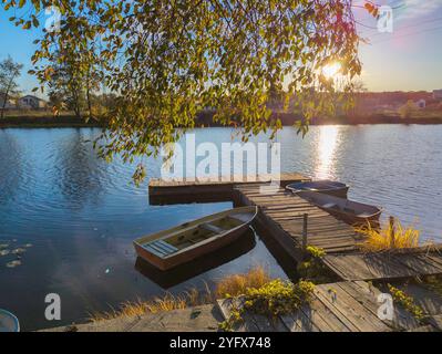 barche al molo sul fiume in autunno. Splendido paesaggio autunnale con laghetto d'acqua e tramonto Foto Stock