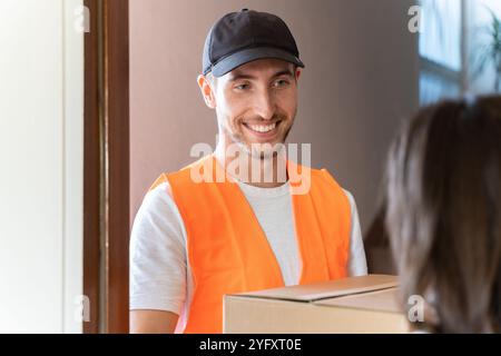 Il corriere consegna il pacco al cliente a casa. Un operatore sorridente che spedisce una scatola di cartone Foto Stock