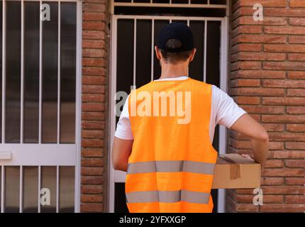 Un uomo giovane e attraente sta lavorando come liberatore di pacchi. Contesto urbano e urbano con il conducente in attesa davanti alla porta del cliente Foto Stock