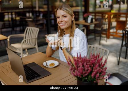 Giovane donna che si gusta un caffè in un caffè con laptop Foto Stock