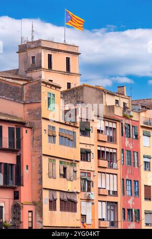 Edifici storici dipinti con colori vivaci lungo il fiume Onyar a Girona, Spagna, caratterizzati da facciate vivaci in colori caldi con una bandiera della Catalogna in cima. Foto Stock