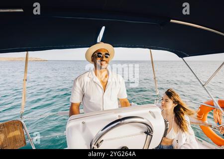 Una coppia si rilassa su una barca sotto il sole, navigando insieme sul mare aperto. La scena cattura un senso di avventura, libertà e divertimento Foto Stock