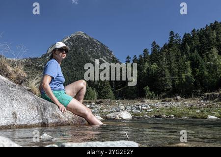 Bella donna ispanica seduta sul bordo di un ruscello di montagna e rinfrescarsi con acqua fredda in una calda giornata estiva. Montagna dei Pirenei spagnoli. Foto Stock