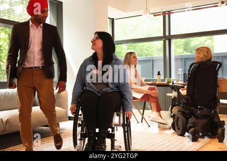 Uomo d'affari che indossa il turbante sikh e donna d'affari su sedia a rotelle in ufficio Foto Stock