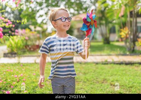 Il ragazzo con gli occhiali sta giocando con la ruota dentata in un giardino Foto Stock