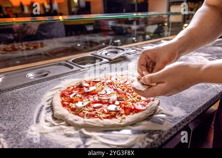 L'uomo prepara la pizza. Cuocere a mano fa una pizza, mette i funghi. Spolverare a mano il formaggio sull'impasto della pizza con salsa di pomodoro, fette di funghi sul Foto Stock