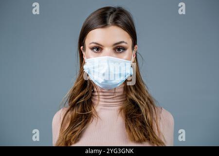Donna che indossa una maschera medica. Donna che indossa la maschera chirurgica per il virus corona. Ragazza in maschera guardando da parte isolato sopra muro grigio Foto Stock