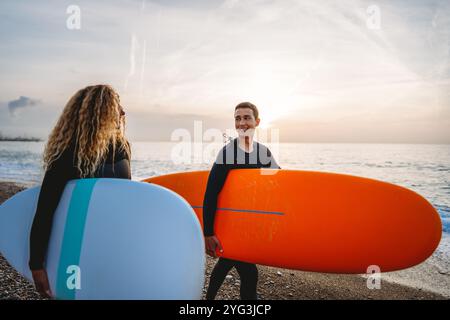 Due giovani surfisti felici con tavola da surf si preparano a colpire le onde al tramonto. Vacanza sportiva attiva Foto Stock