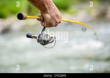 Pescatore con filatura sul fiume. Pescatore che tiene a mano la canna da pesca con la bobina. Mulinello da pesca. Foto Stock