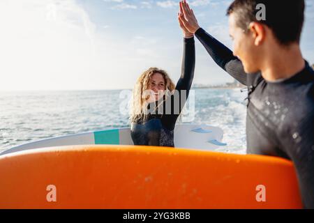 Due giovani surfisti felici con tavola da surf si preparano a colpire le onde al tramonto. Vacanza sportiva attiva Foto Stock