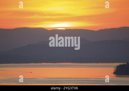 Tramonto dietro una catena montuosa lontana su un lago tranquillo, toni caldi, Hegne, Allensbach, lago di Costanza, Baden-Wuerttemberg, Germania, Europa Foto Stock